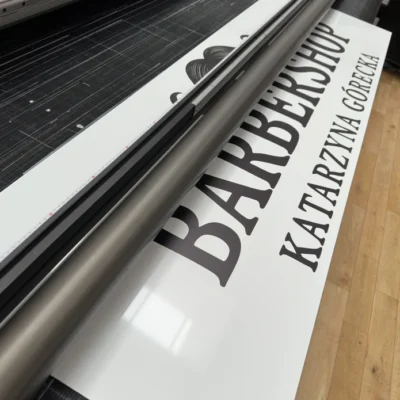 Reklamowy szyld dla barbershopu z czarnym napisem, drukowany na Dibondzie metodą UV