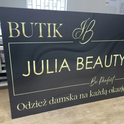 Tablica wykonana z czarnego Dibondu z eleganckim złotym nadrukiem UV, szyld dla butiku odzieżowego