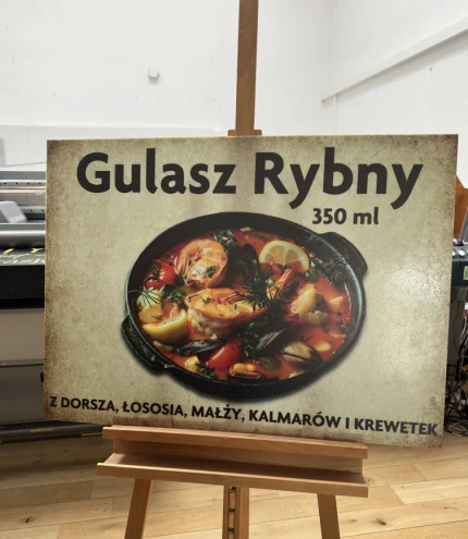 Schild mit dem Gericht „Fischgulasch”, Grafik einer Fischsuppe auf Plexiglasplatte