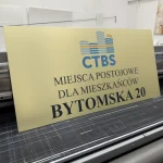Szyld reklamowy UV na złotym dibondzie z nadrukiem tekstowym i logo