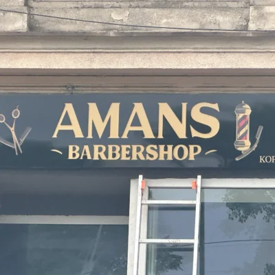 Czarny kaseton z Dibondu – AMANS Barbershop, złote elementy graficzne