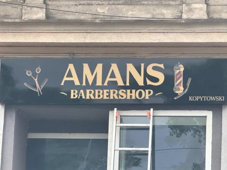 Czarny kaseton z Dibondu – AMANS Barbershop, złote elementy graficzne