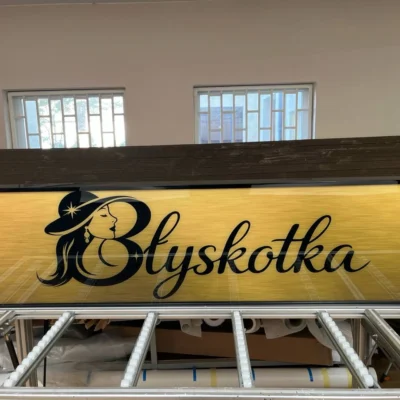 Szyld LED „Błyskotka” na żółtym tle, czarna typografia i logo, ujęcie z przodu w pracowni