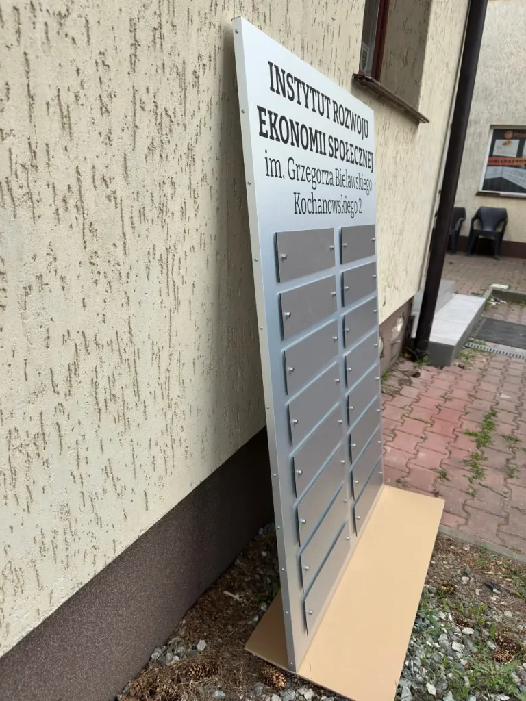 Tablica informacyjna zbiorcza Dibond ustawiona przy elewacji